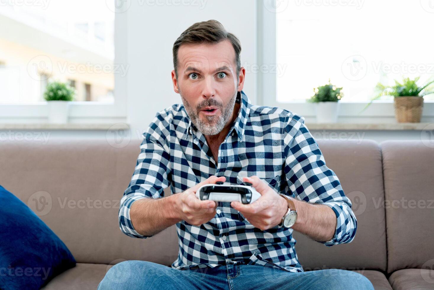 A man is sitting on a couch holding a game controller photo