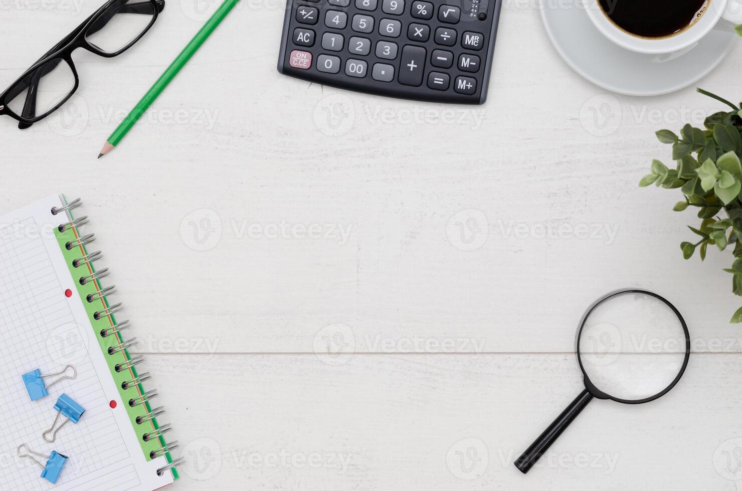 Top view of office desk with calculator, pen, glasses, and a plant photo