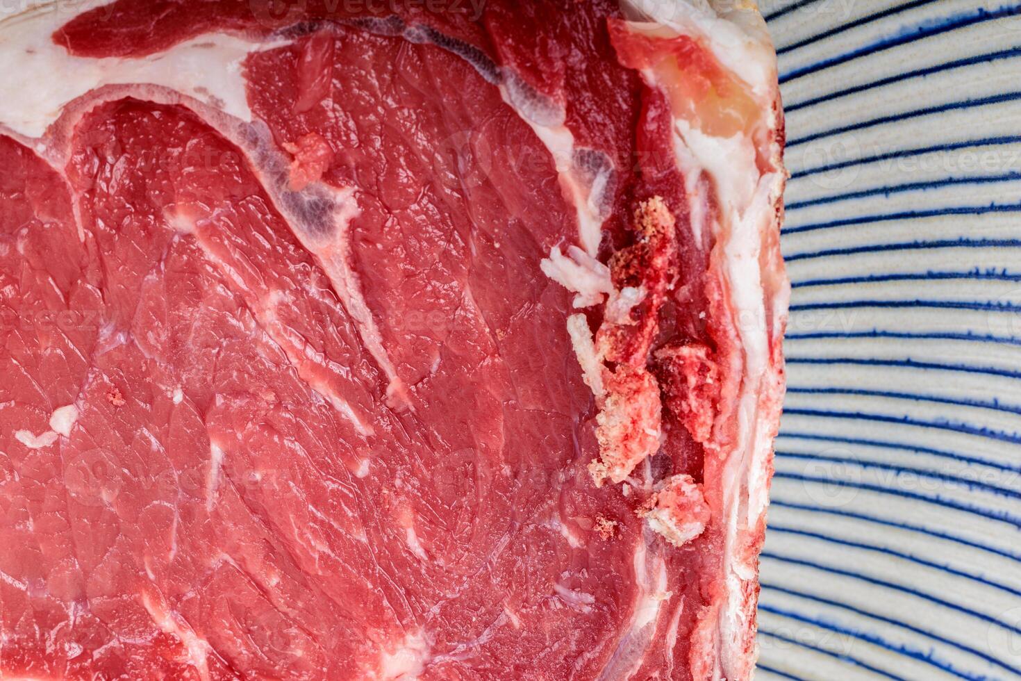 Raw beef rib steak detail on a striped ceramic plate. photo