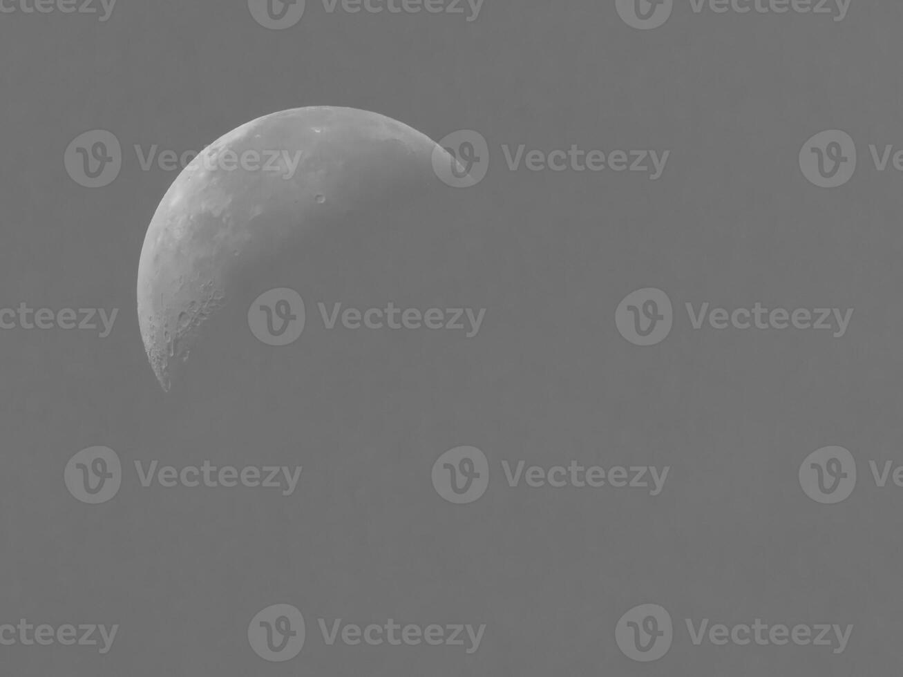 Half moon in detail with visible craters against a soft gray sky. photo