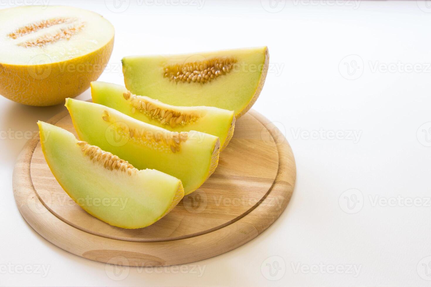 Fresh cantaloupe slices arranged neatly on a wooden cutting board, with the whole fruit beside them. The yellow rind contrasts with the juicy green flesh, making it an appealing summer treat. photo
