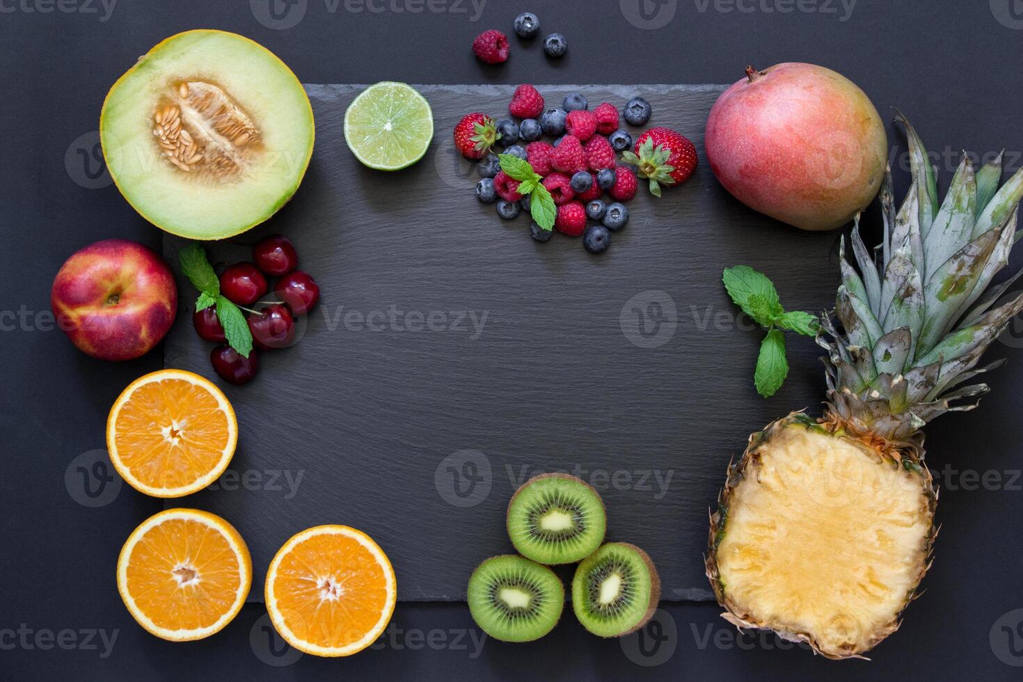 Rectangle of pineapple, mango, kiwi, oranges lime, melon, nectarine and cherries strawberries, blueberries, raspberries in center empty space on black background. Fruits berries rectangle. Horizontal. photo