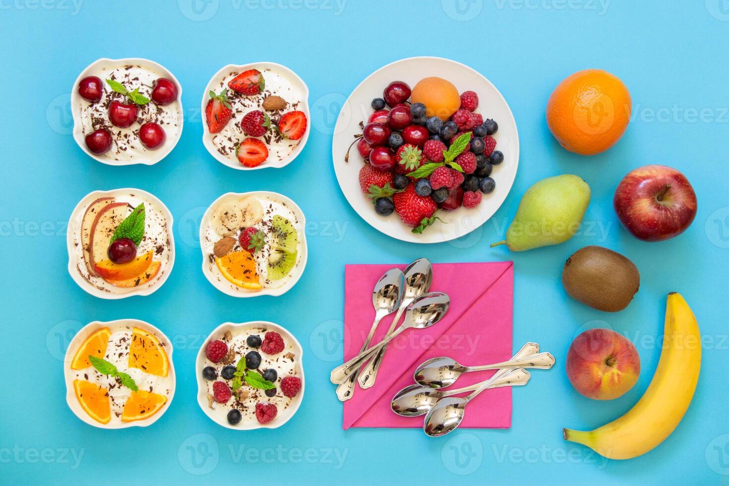 6 bowls of differently dressed yogurts displayed vertically in 2 rows of 3 pc. near plate of berries, fruits, 6 spoons, napkins on blue background. Six yogurts ready to eat and ingredients. Top view. photo