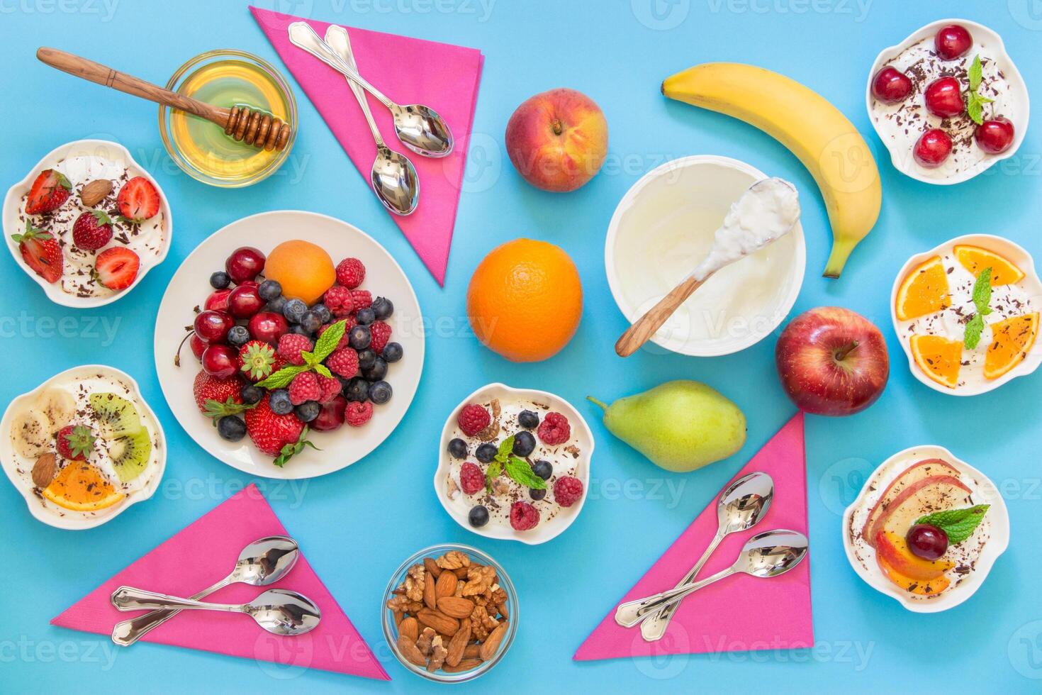 6 bowls of yogurt dressed with different ingredients fruit, berries, nuts, honey, and 6 spoons, napkins on light blue background. Six differently dressed yogurts and ingredients. Horizontal. Top view. photo