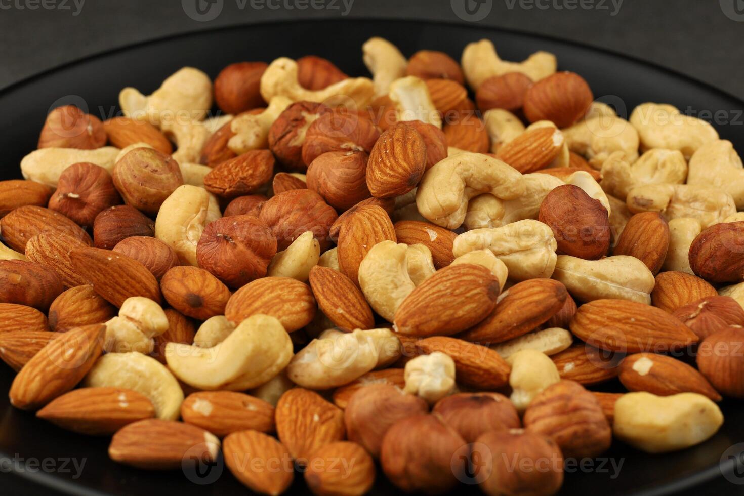 Mixed nuts assortment on a black plate with almonds, cashews, and hazelnuts arranged for snacking options photo
