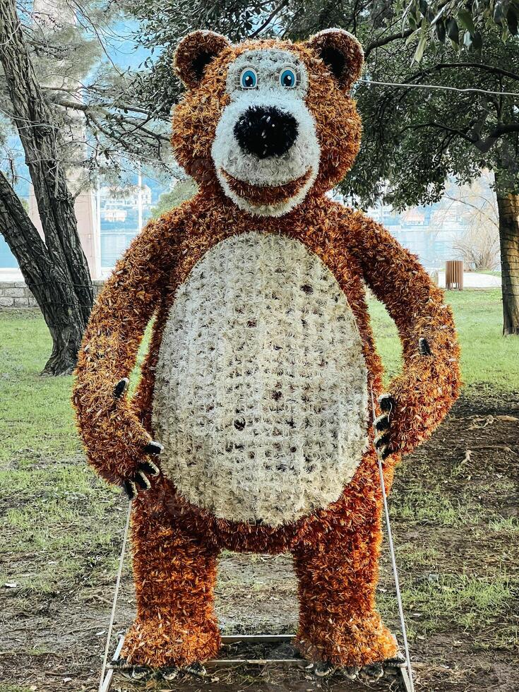 Fluffy figure of a smiling bear stands near the trees in a clearing photo