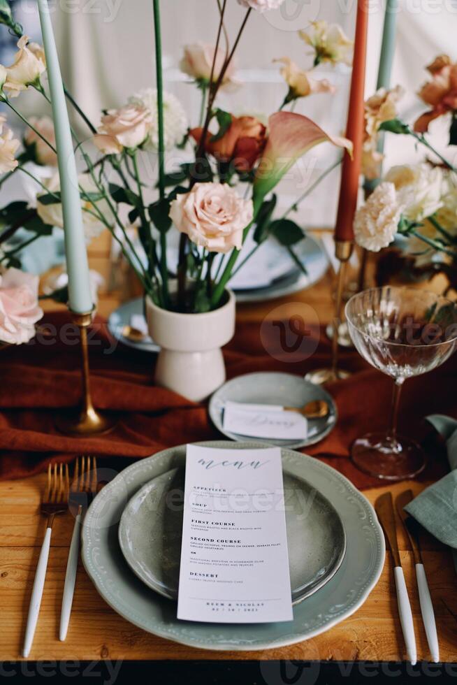 Festive menu lies on a plate on a served table near a bouquet of flowers photo