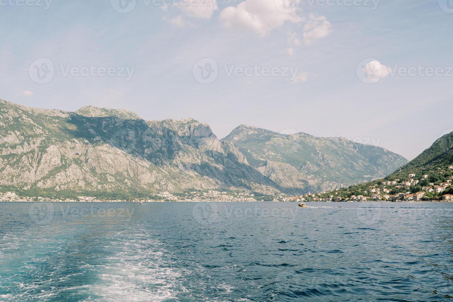 White foam trail on the blue sea from a passing motor boat against the backdrop of a mountainous coast photo
