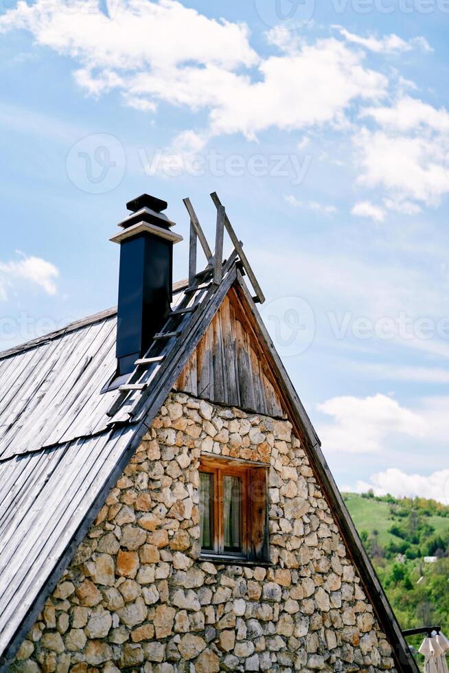 Triangular roof of a stone house with stairs and chimney against a cloudy sky photo