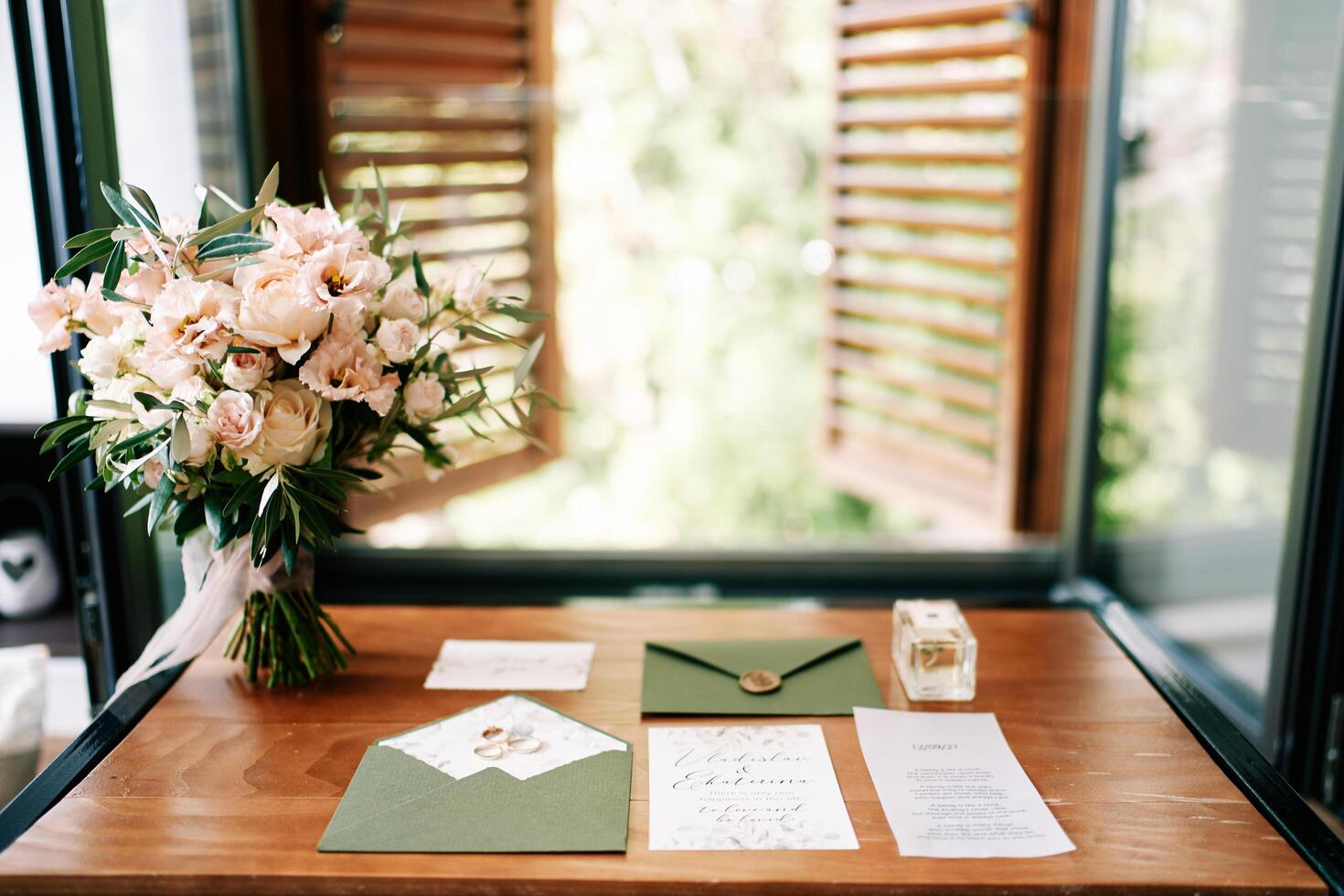 Montenegro, Budva - March 09, 2024. Bouquet of flowers stands near invitations and wedding rings on a wooden table by the window photo
