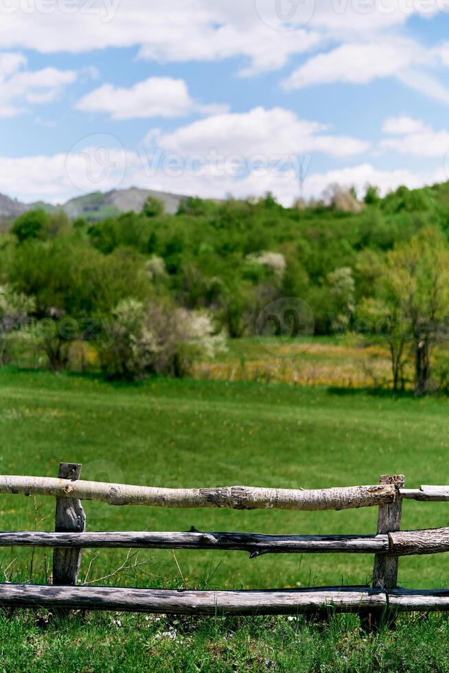Wooden fence on a green field with mountains in the background photo