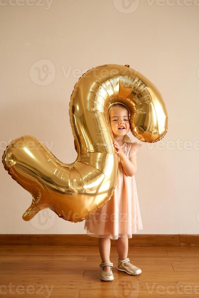 Little girl stands in a room with an inflatable number two in her hands photo