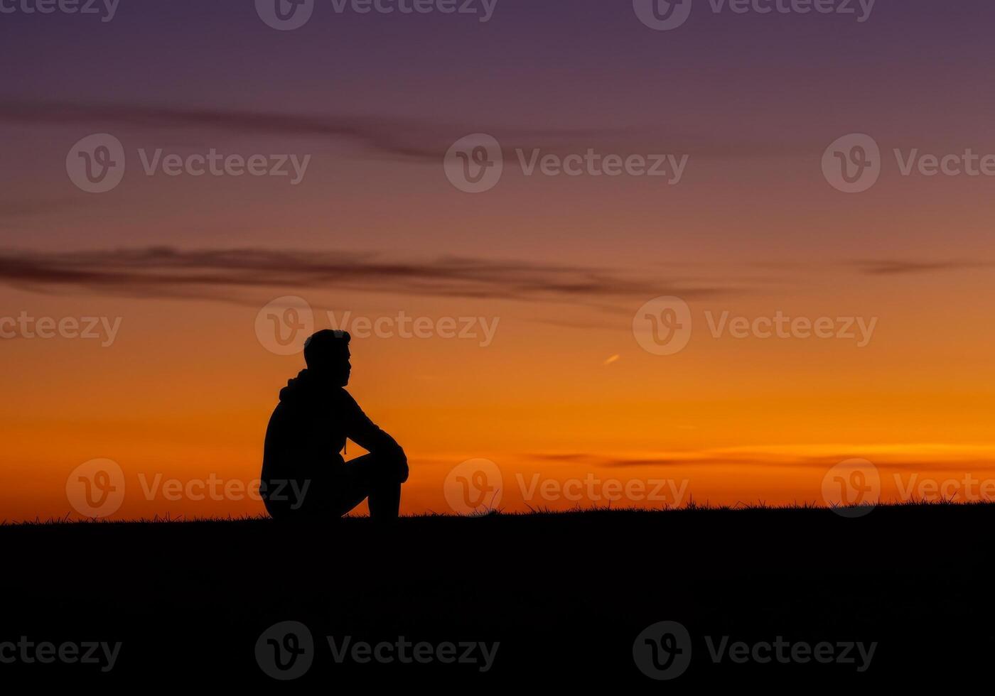 Silhouette of Man Sitting on Hill Gazing at Vibrant Orange Sunset photo