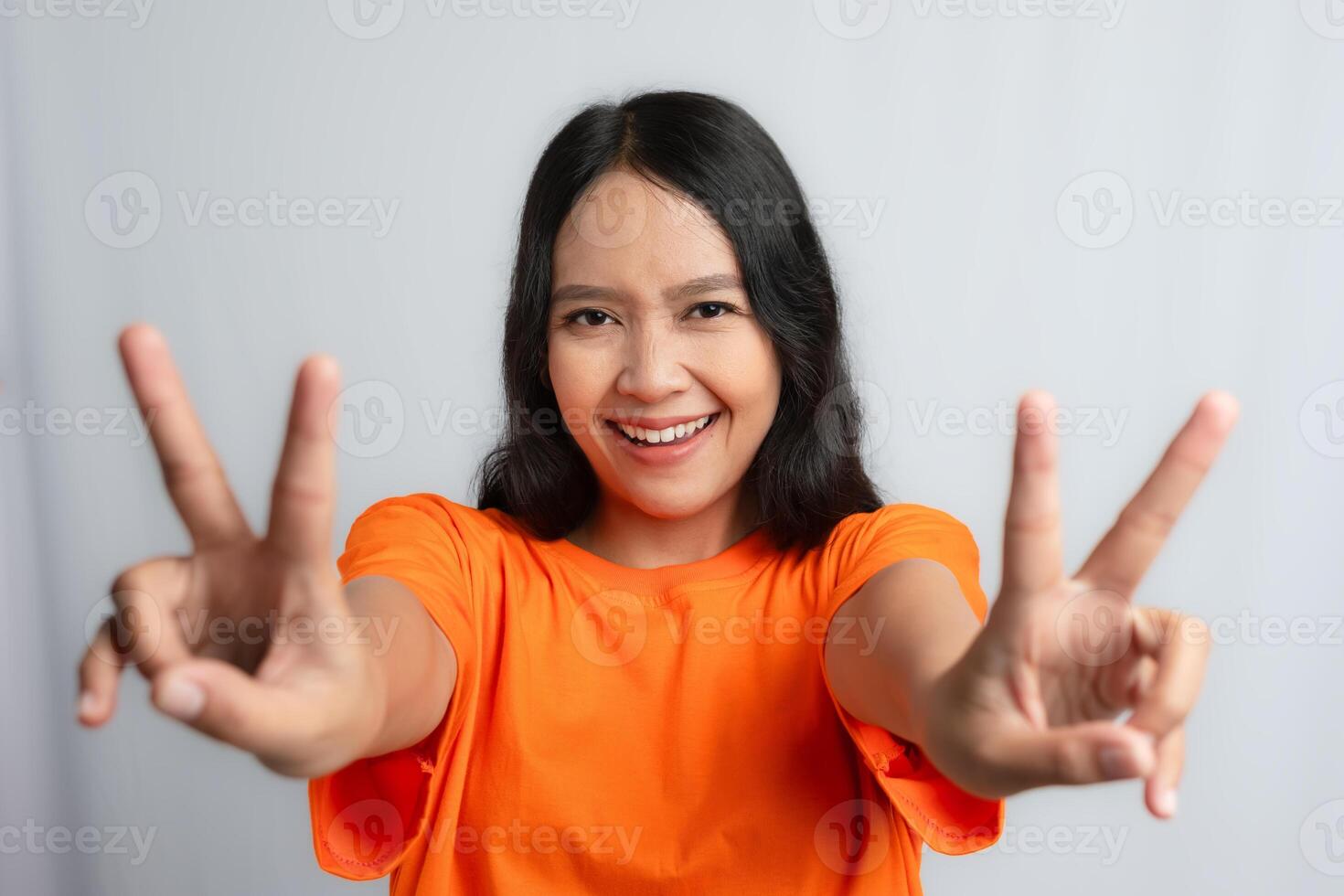 A woman smiling and showing peace signs with both hands by wearing orange tshirt photo