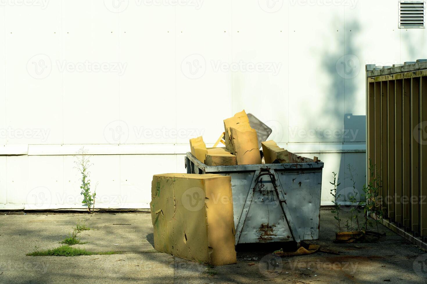 Waste Container Filled with Large Yellow Foam Pieces Near White Wall photo