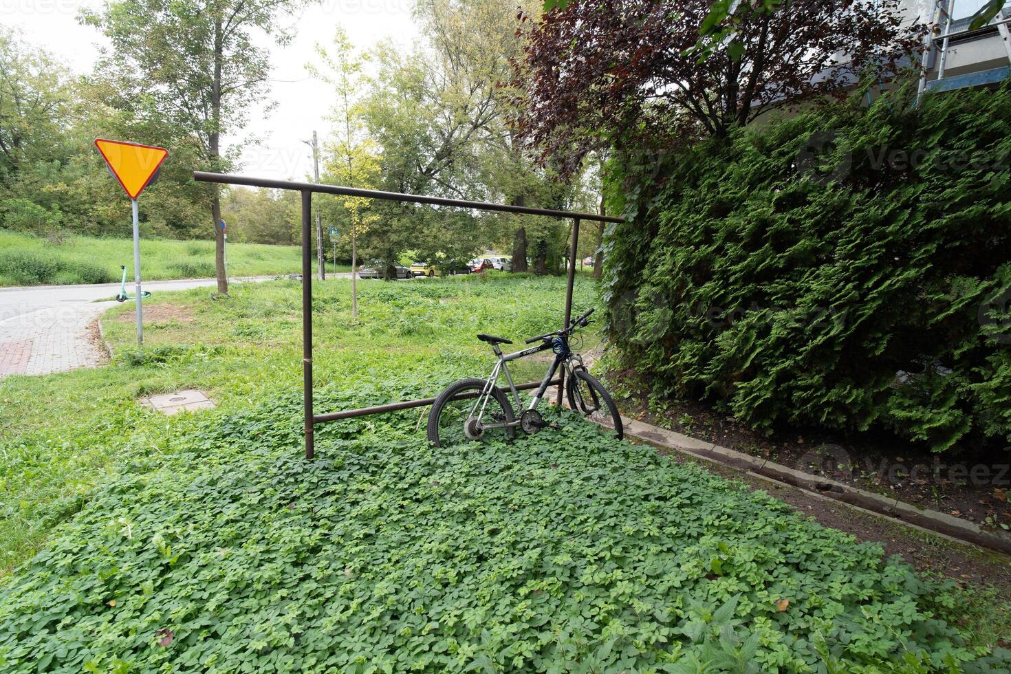Bicycle Parked on Grass Field Next to Bushes with Road Sign in Background photo