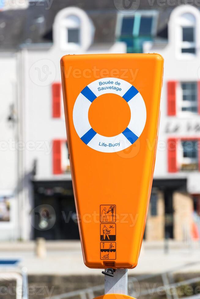 Bright orange life buoy station with safety symbols in a harborside setting photo