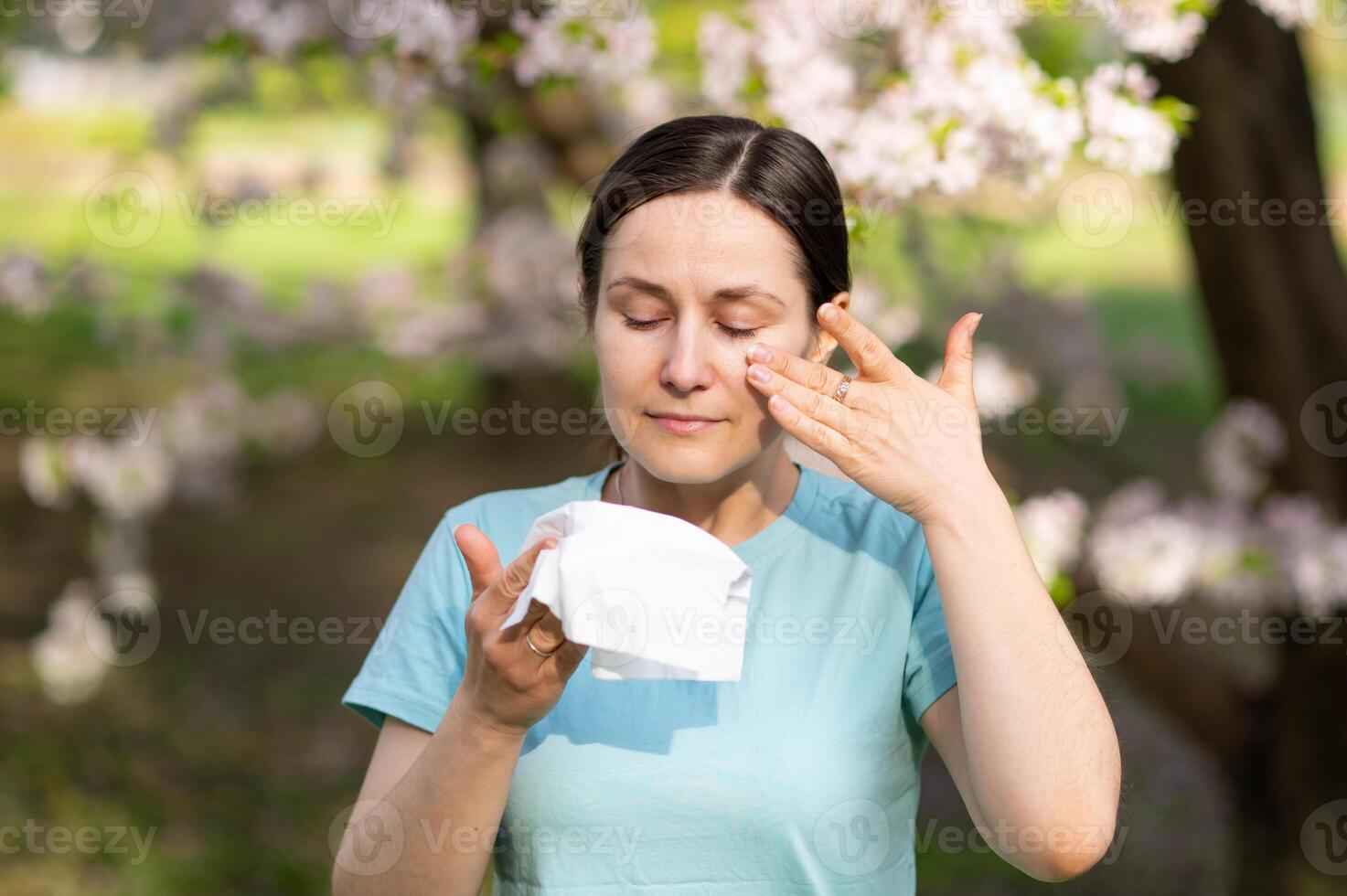A woman is blowing her nose in front of a tree photo