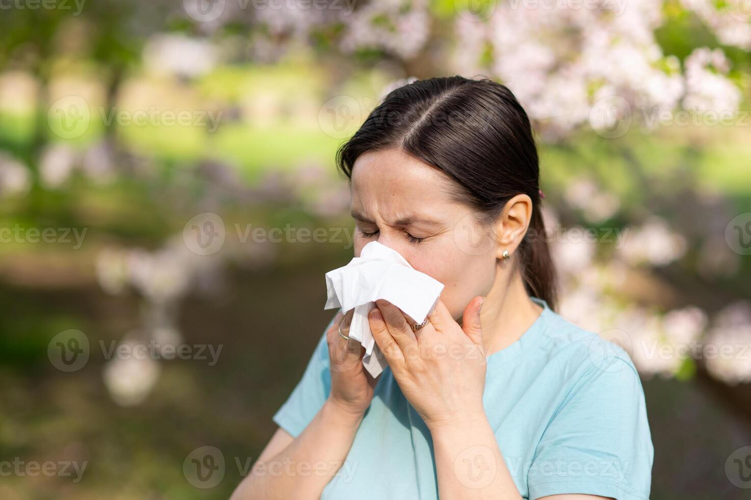 A woman blowing her nose in front of a tree photo