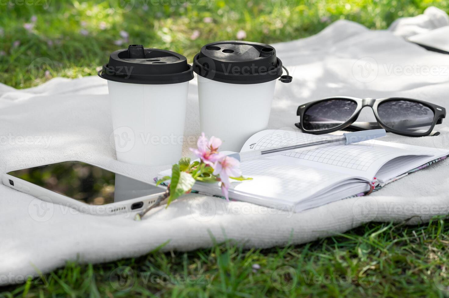 Two coffee cups, sunglasses, notebook and phone on the grass photo