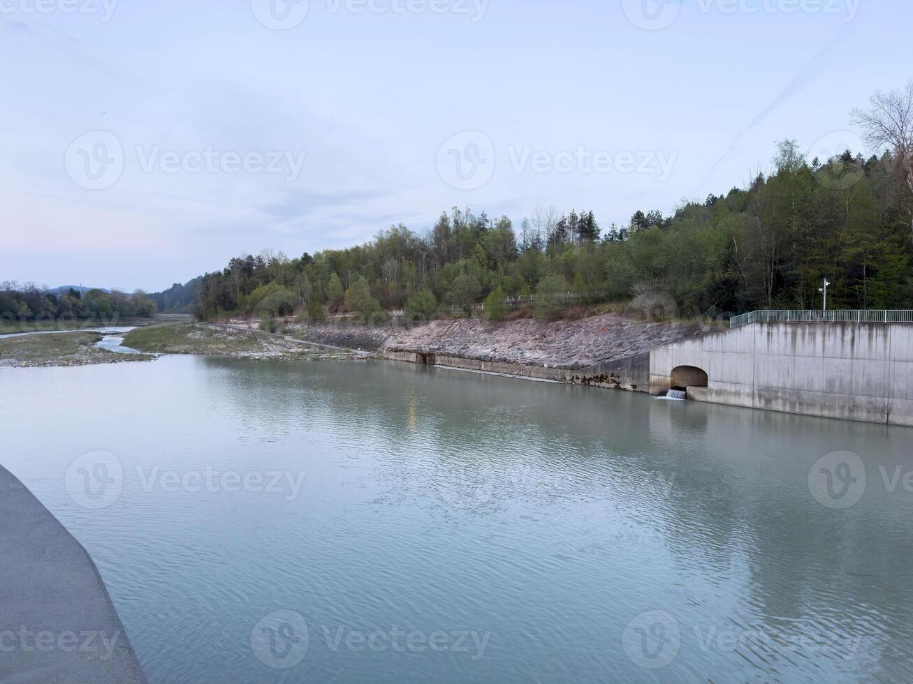 Serene riverside with forest background and concrete structure at dusk photo