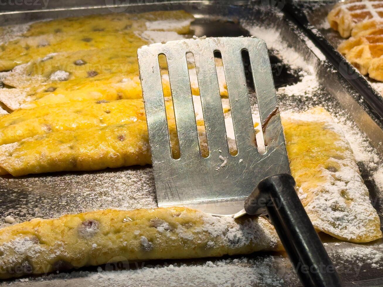Powdered sugar-covered crepes with spatula on griddle photo