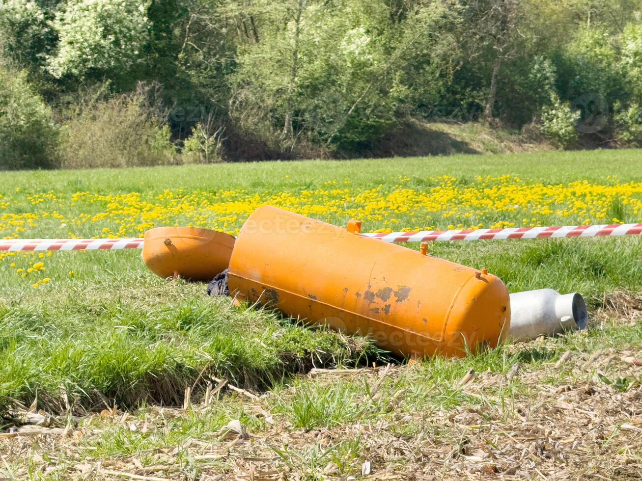 Orange gas cylinder in field with caution tape and lush greenery background photo