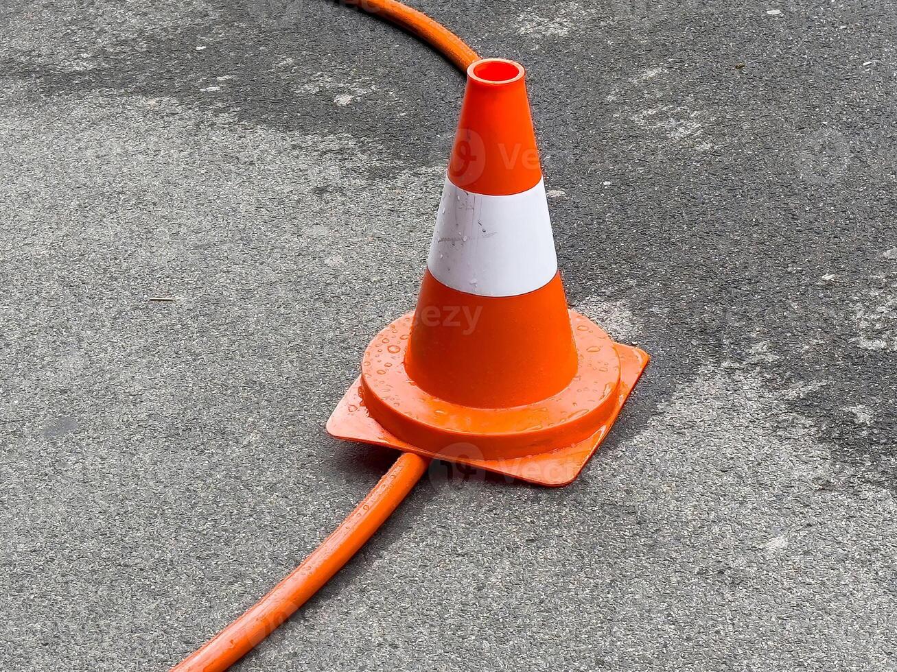 Orange traffic cone on wet asphalt with cable passing through base photo