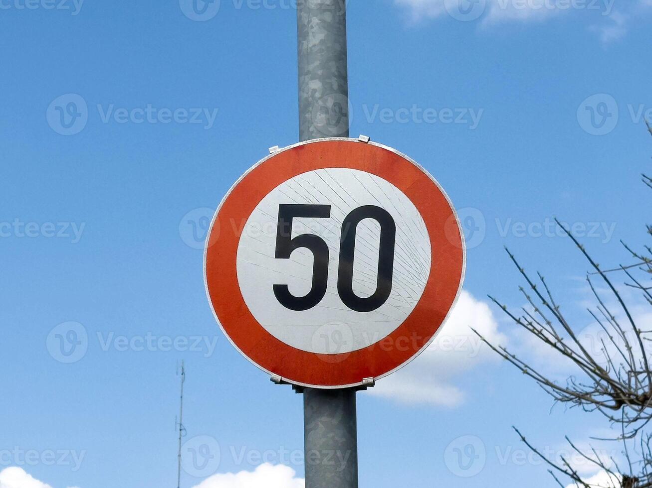 Red and white circular 50 km h speed limit sign against blue sky photo