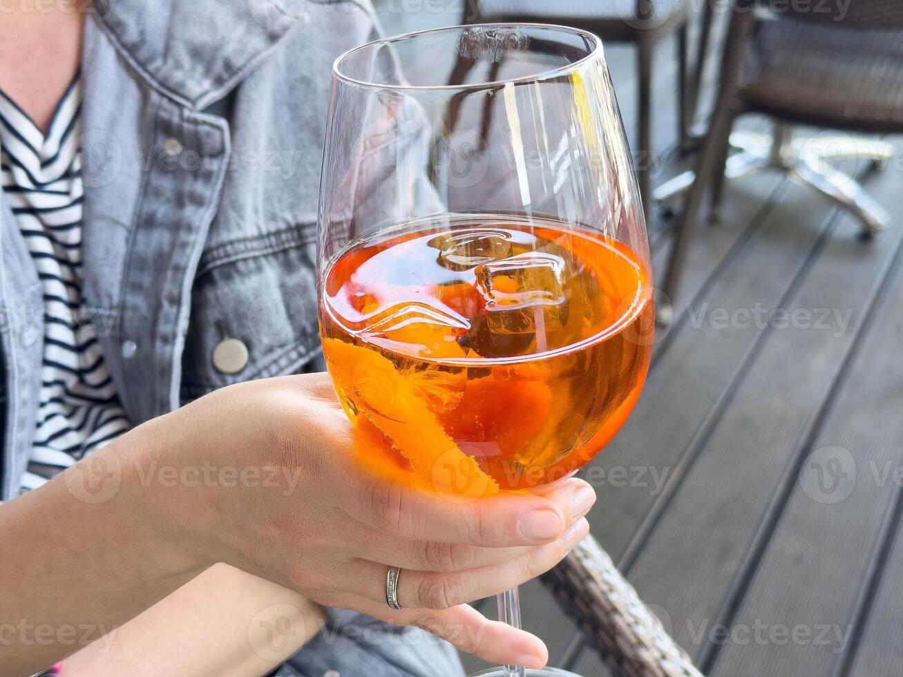 Female hand holding aperol spritz with ice on outdoor patio in casual setting photo