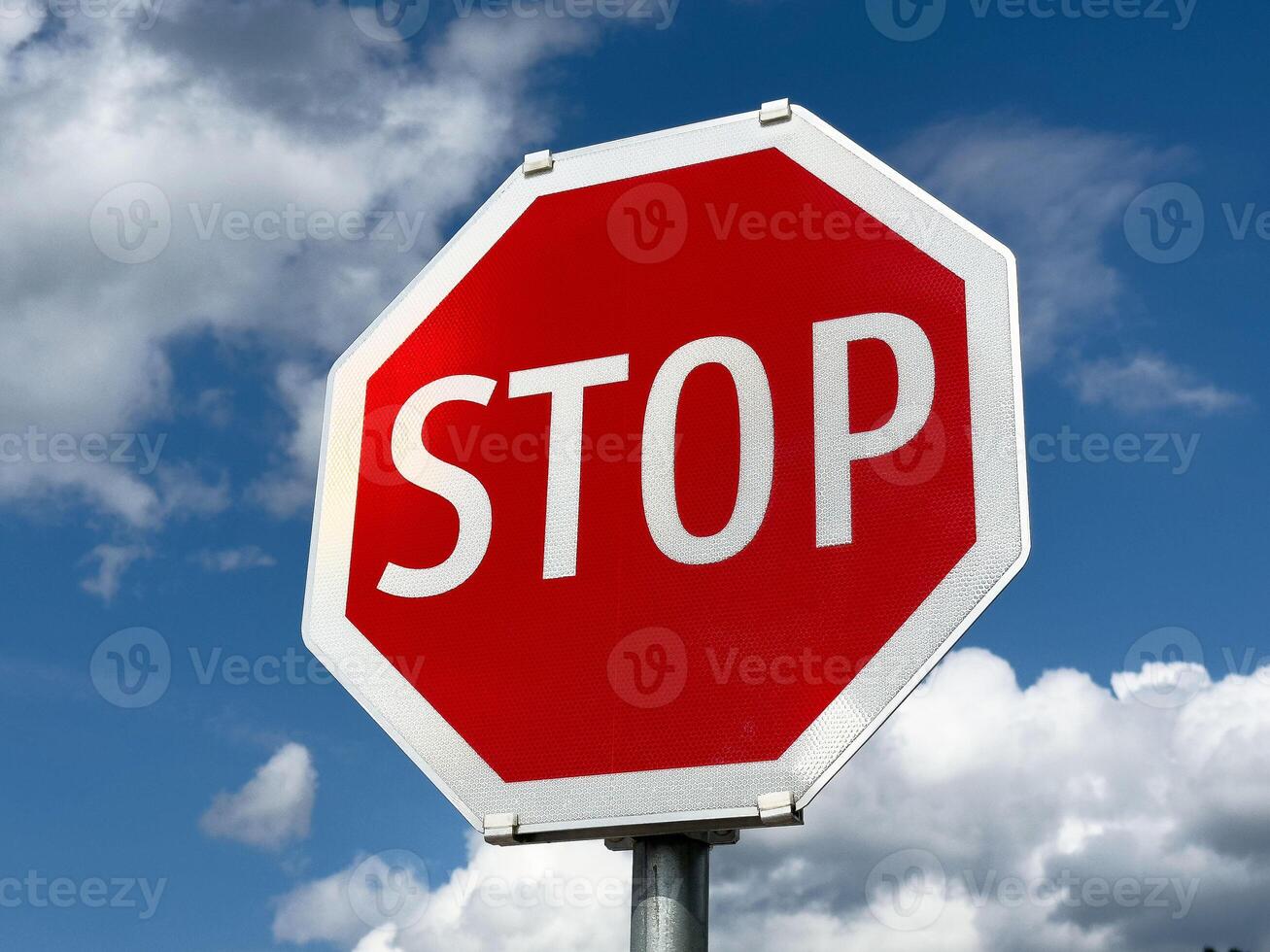 Bright red stop sign against blue sky and clouds photo