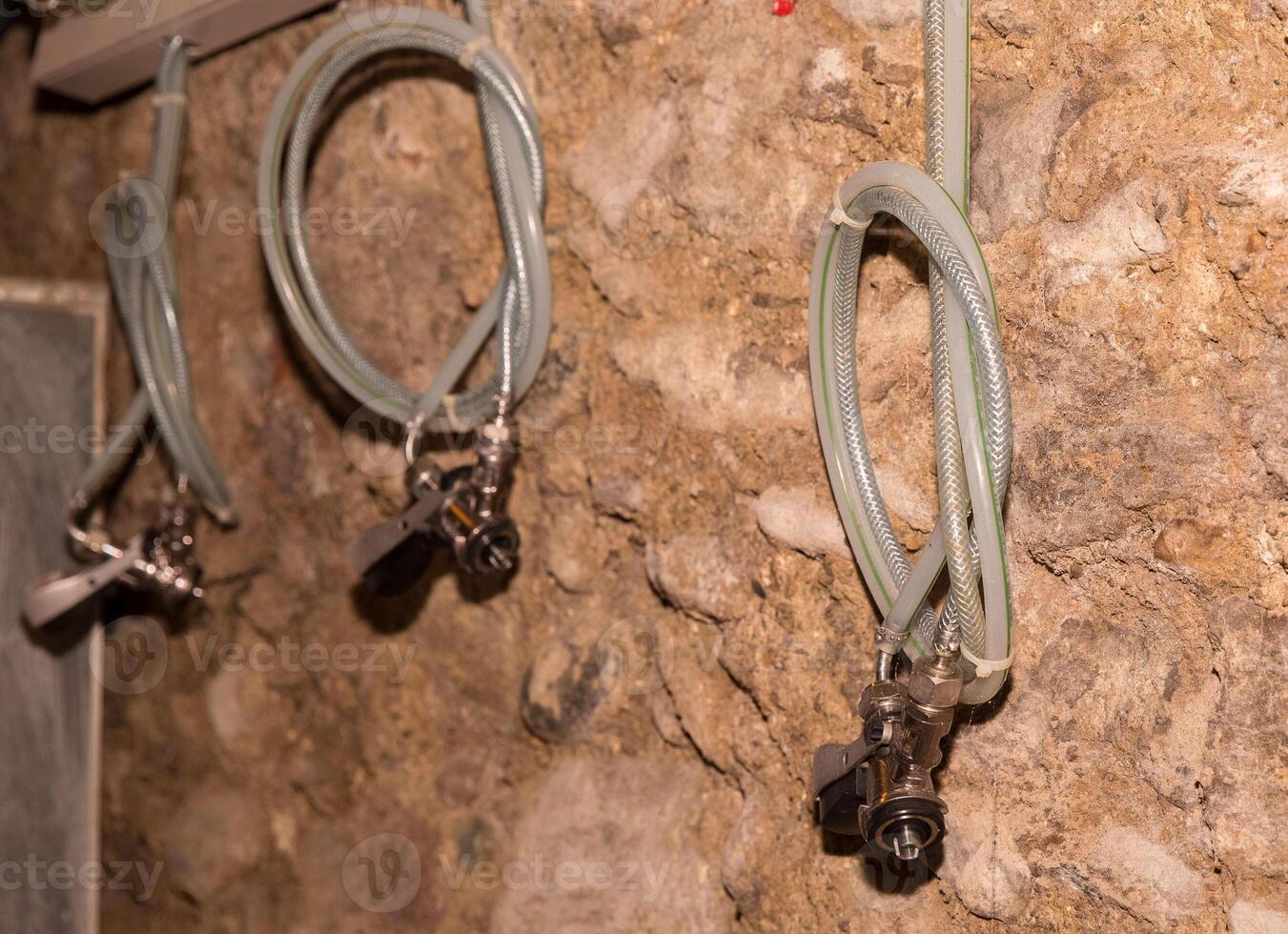 Industrial hoses on stone wall with metal connectors in a basement setting photo
