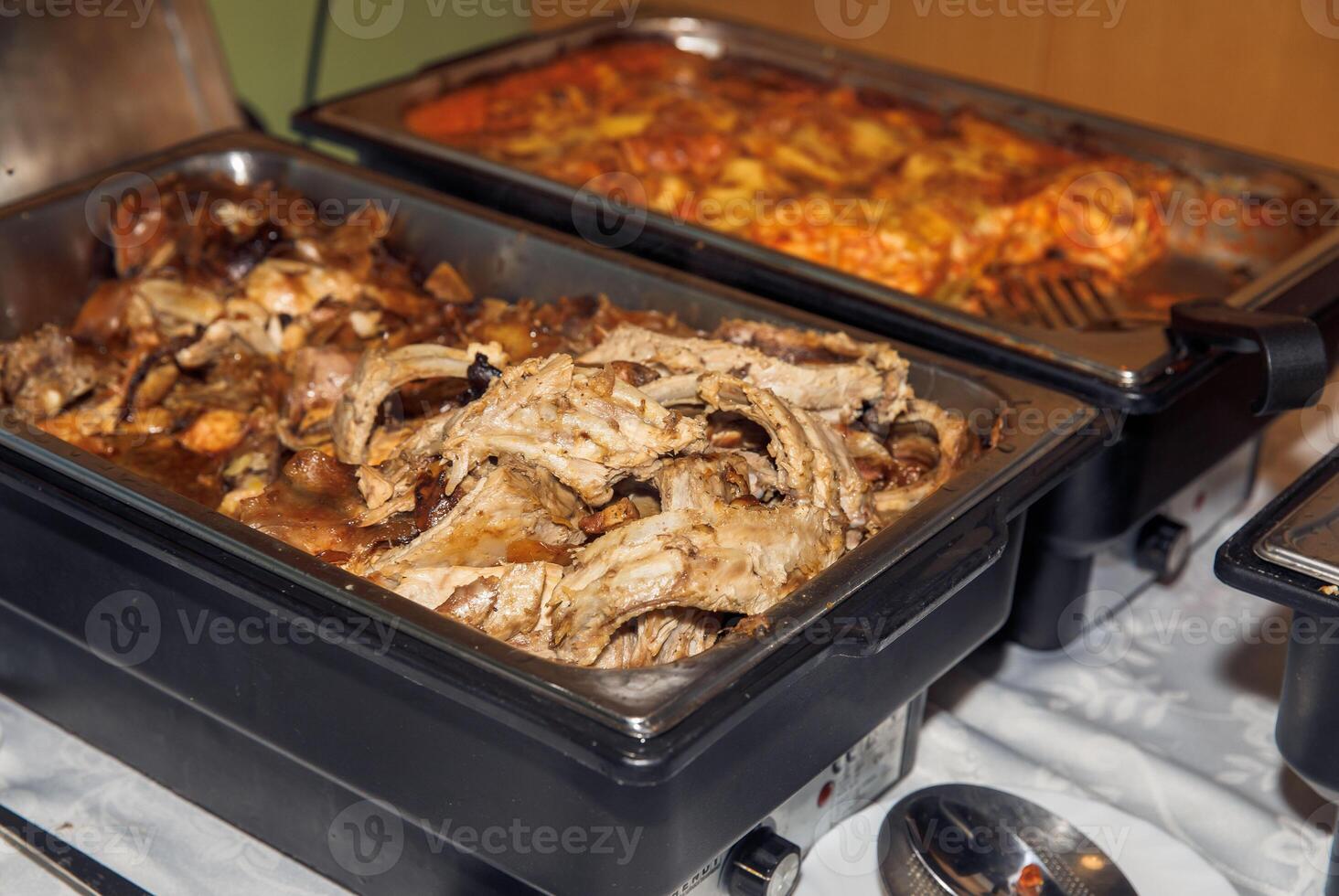 Buffet style tray with cooked pork ribs and cheesy potato casserole at catered event photo