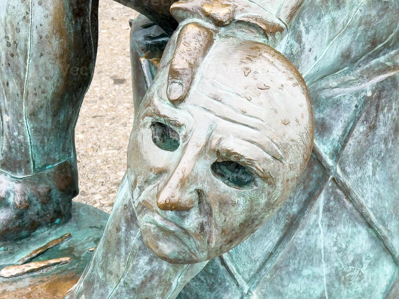 Bronze sculpture of a jester holding a mask with intricate details photo