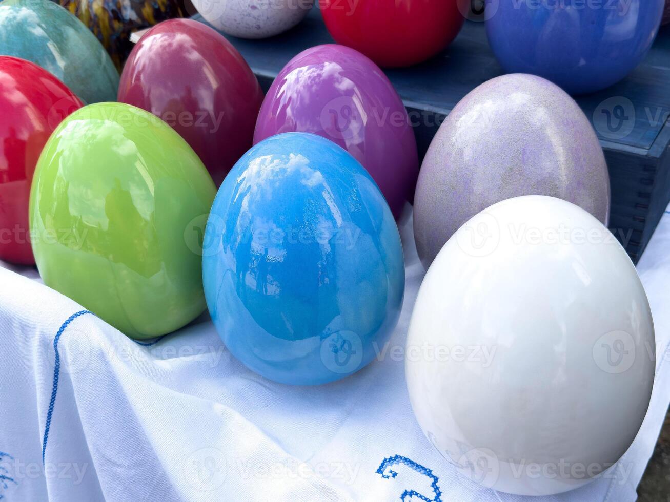 Colorful display of glazed ceramic eggs on white fabric tablecloth photo