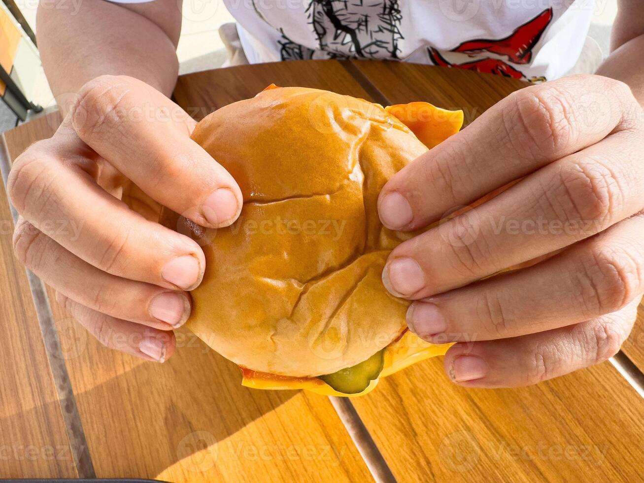Close-up of hands holding a cheeseburger on a wooden table photo