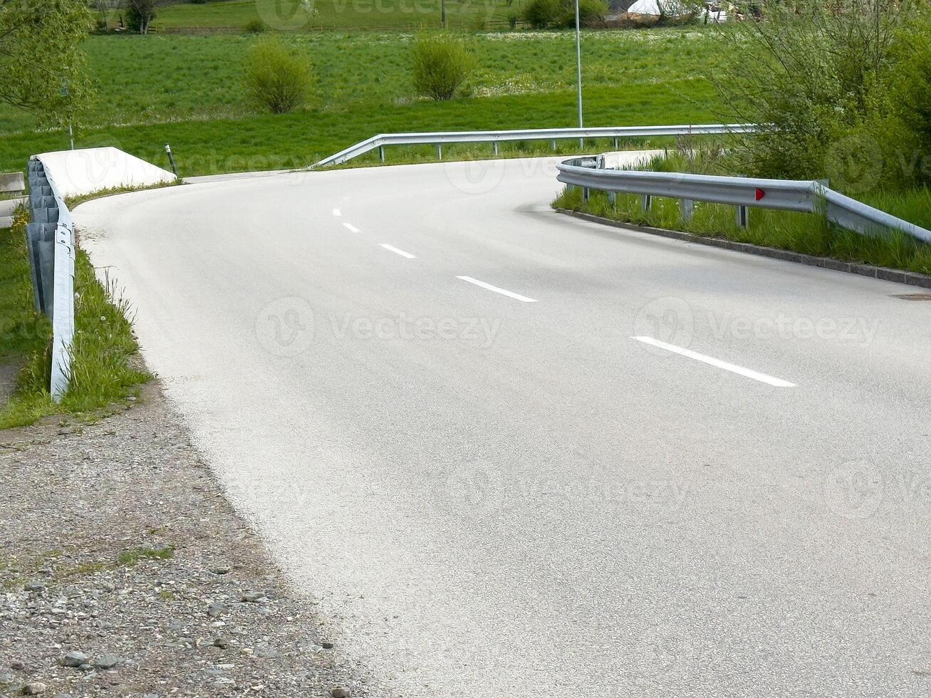 Empty country road with green fields and guardrails in serene landscape photo