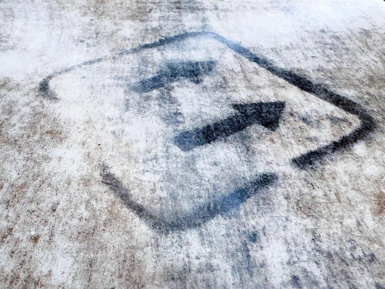 Weathered directional arrow sign on rustic concrete surface photo