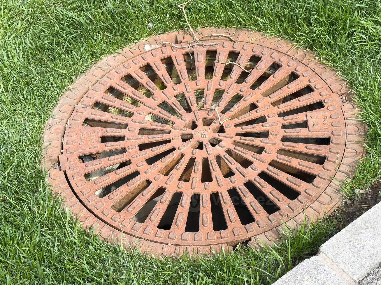 Round metal manhole cover on grass with circular pattern and letters photo