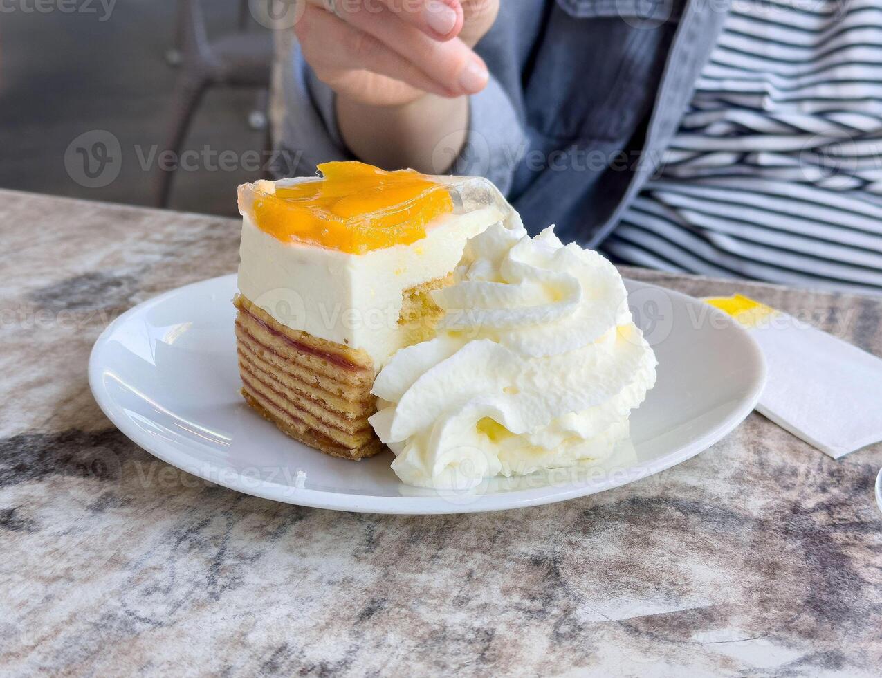 Female enjoying delicious mango cream cake with whipped topping at cafe photo