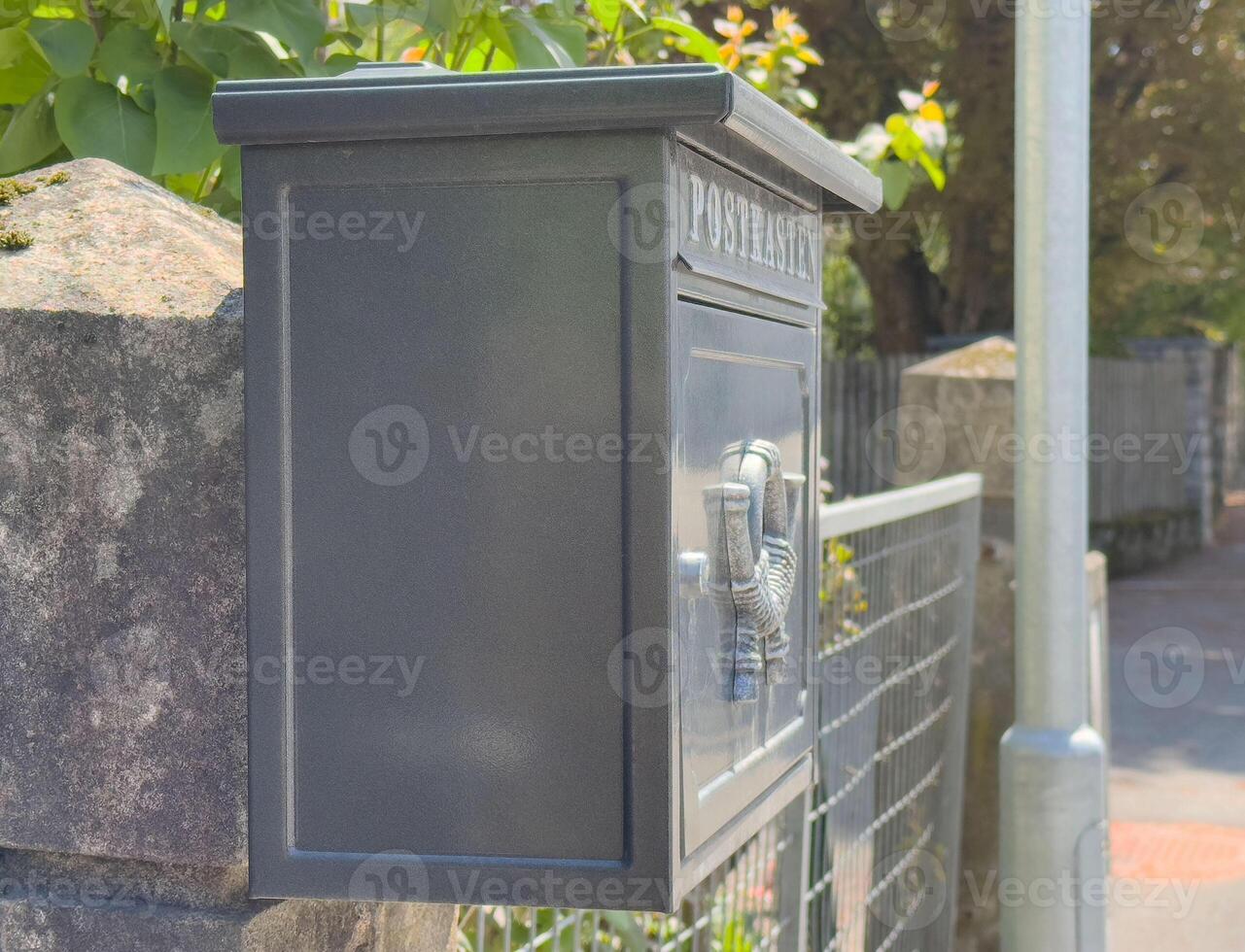 Black metal mailbox on stone wall in sunlit suburban street photo