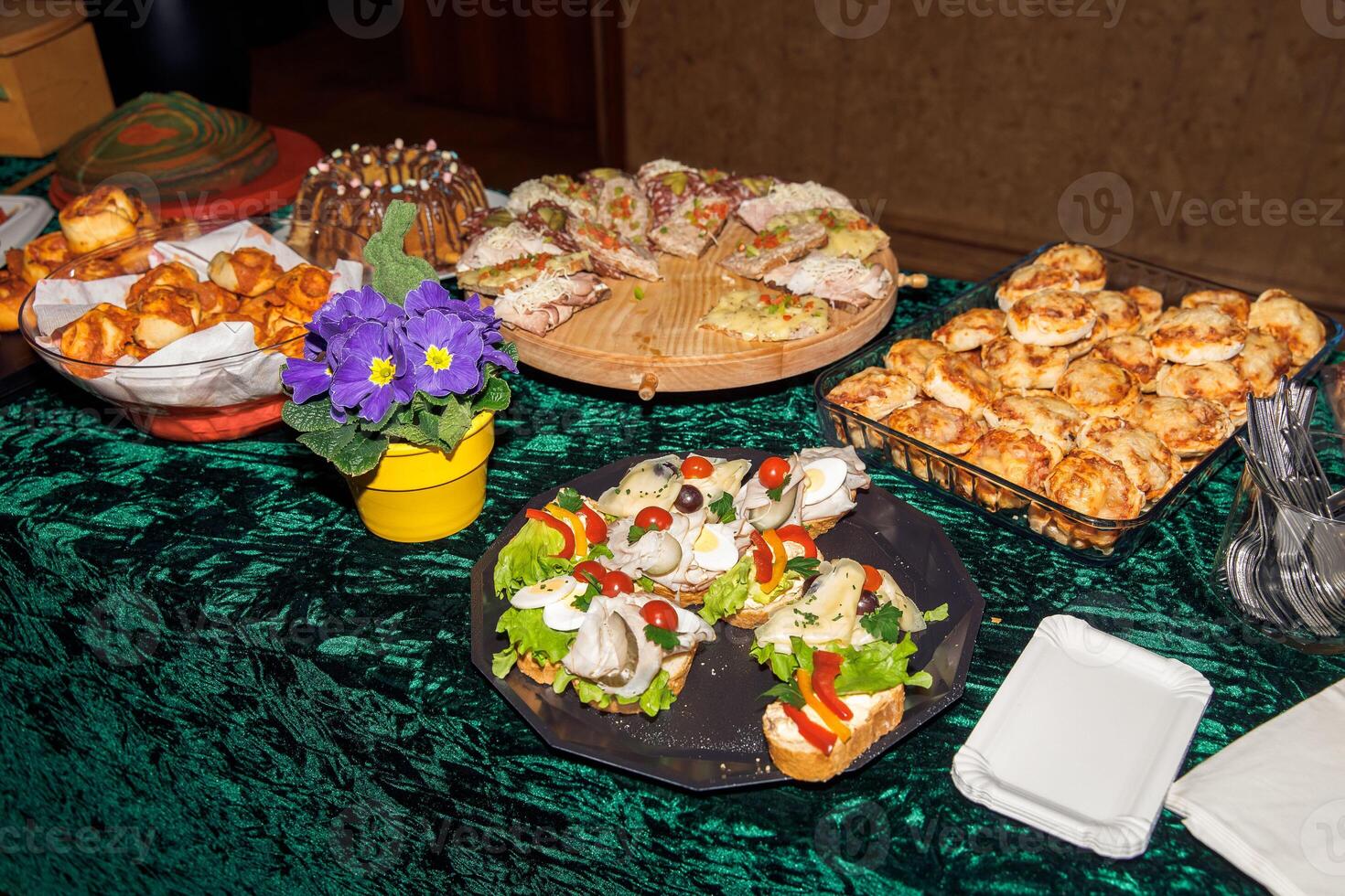 Assorted pastries and sandwiches on green tablecloth with potted purple flowers photo