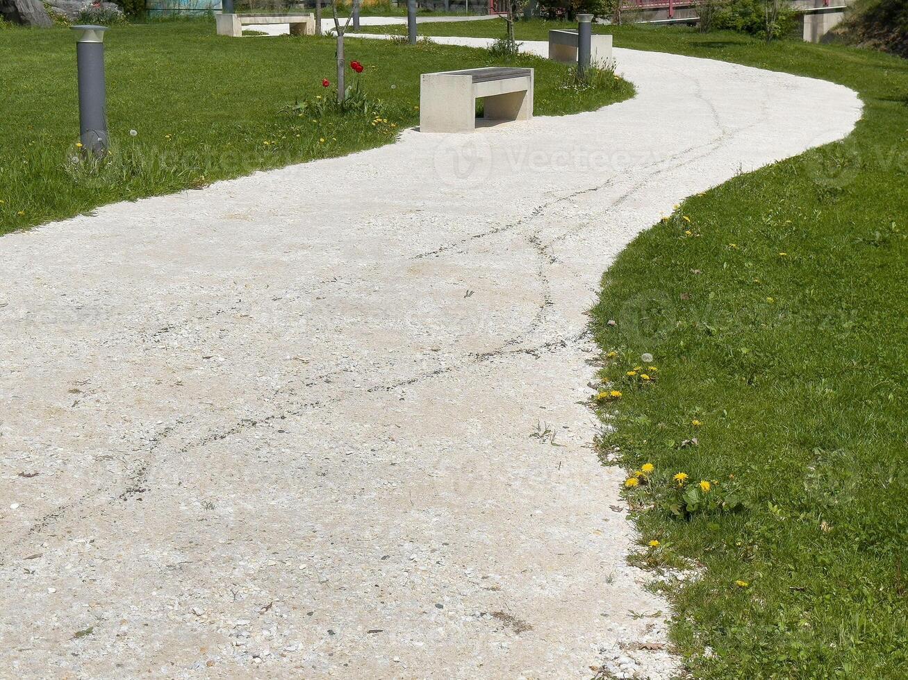 Serene park pathway with lush greenery and concrete benches on a sunny day photo