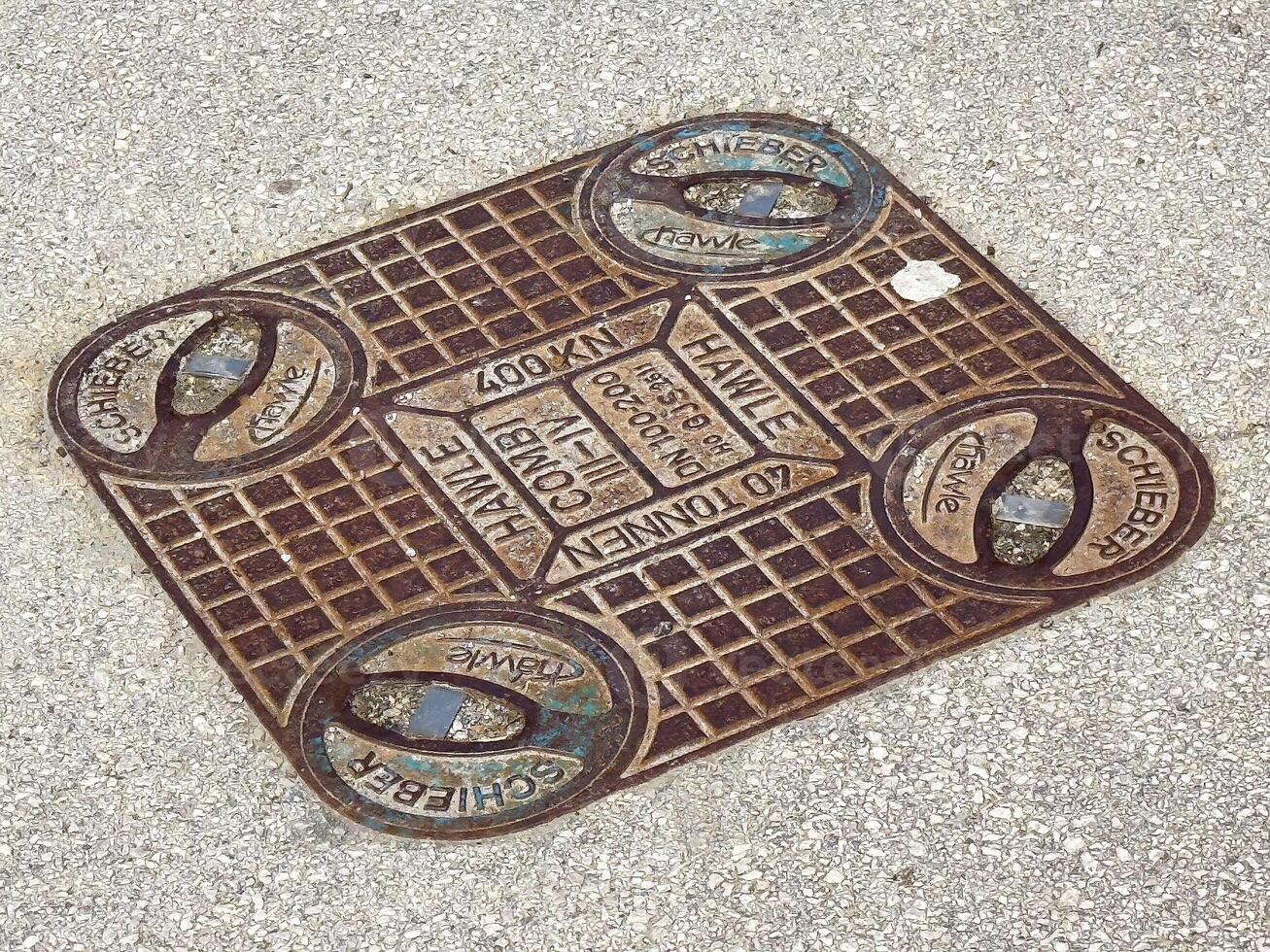 Rectangular metal manhole cover on concrete surface with brand names photo