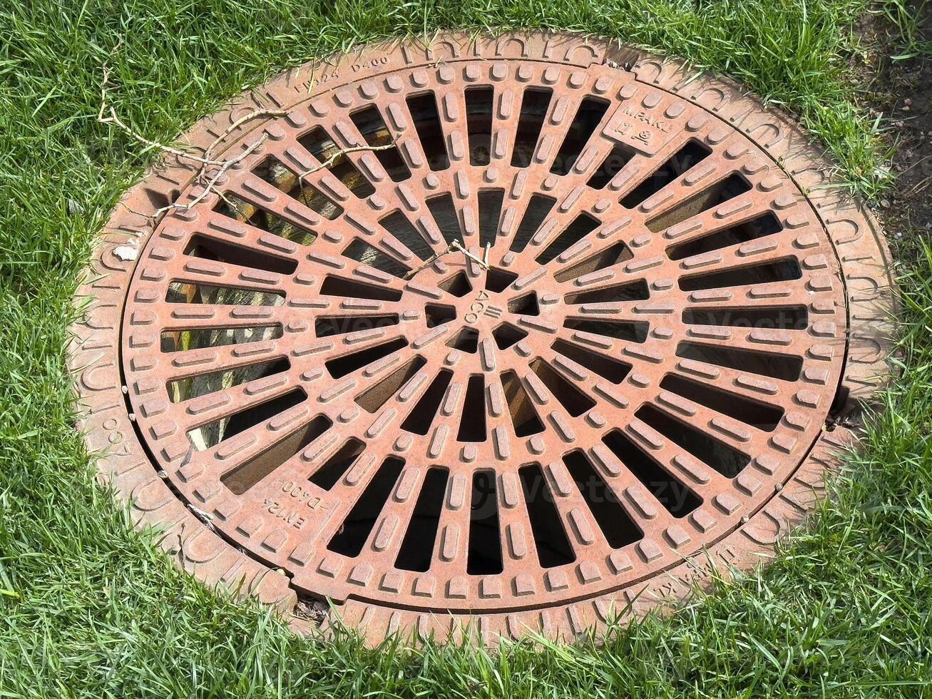 Round iron manhole cover on grass surface in urban environment photo