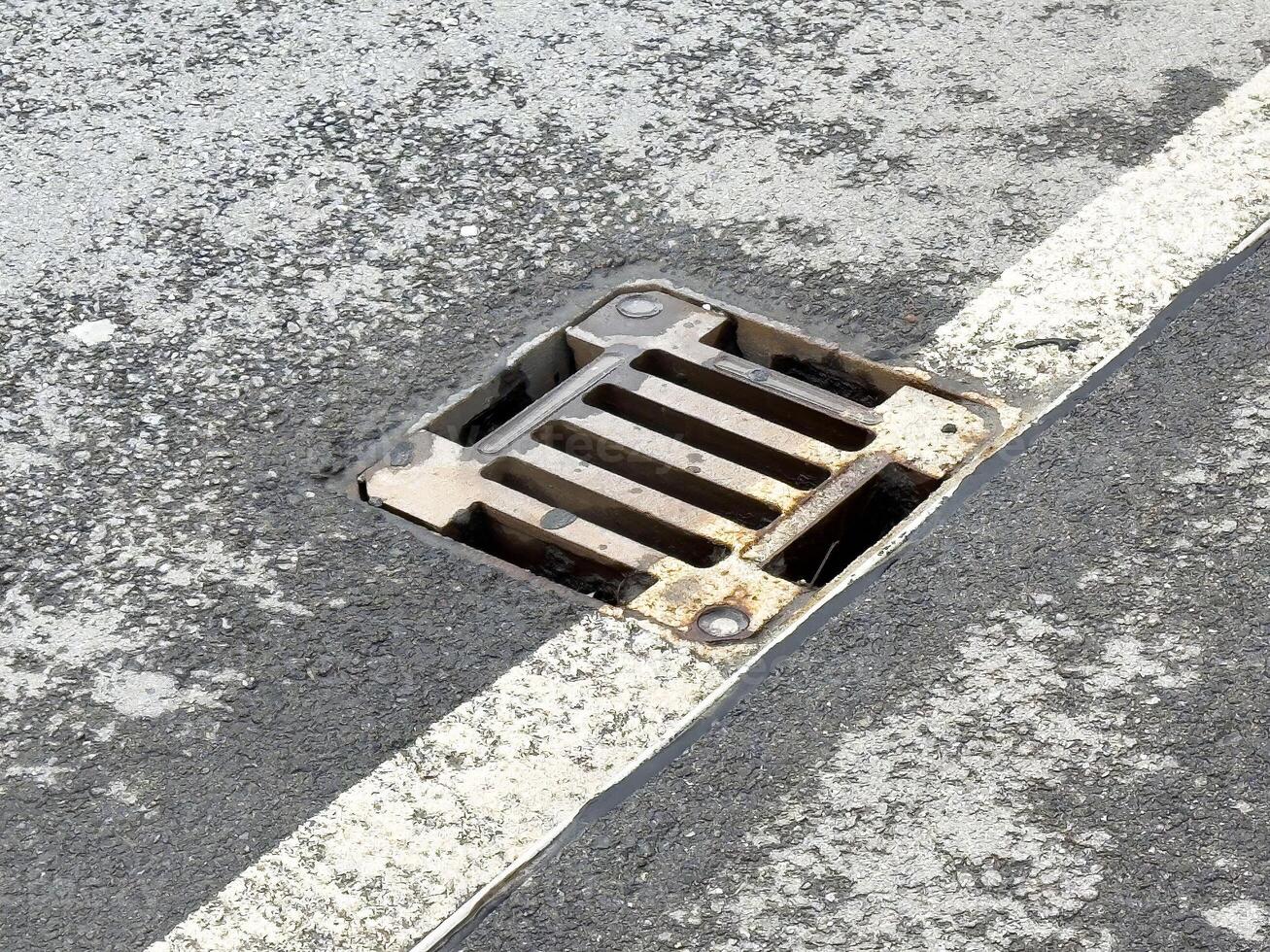 Rusty roadside drain on weathered asphalt with white line photo