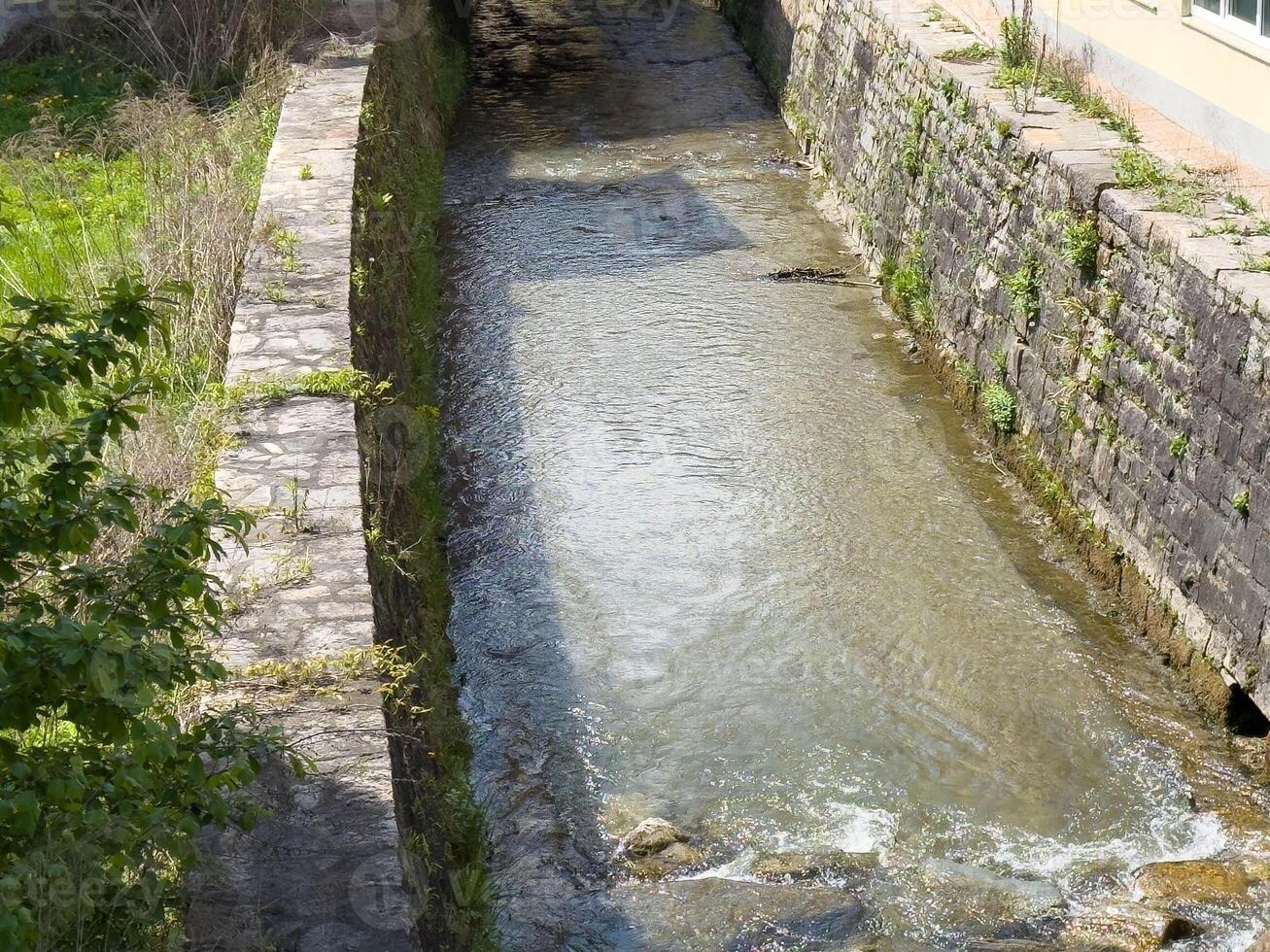 Serene stone-lined canal with flowing water in a green urban setting photo