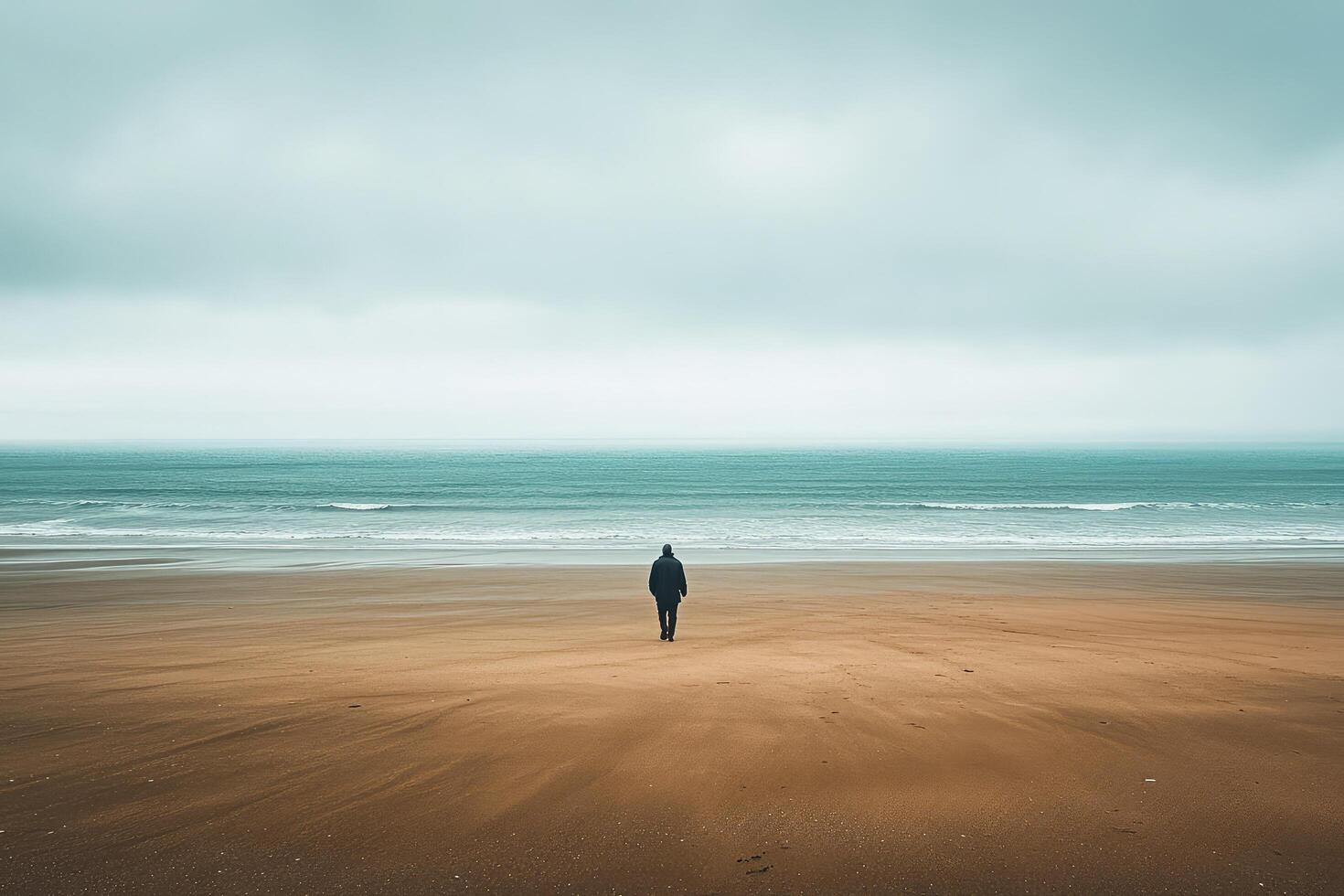 A lone person standing on a beach in front of the ocean photo