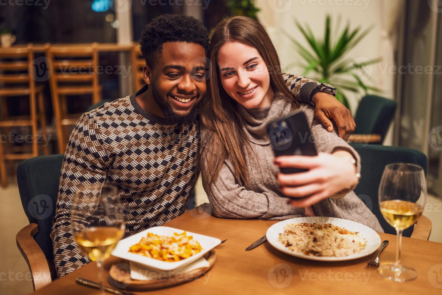 Joyful couple enjoying a casual restaurant date, laughing together while snapping selfies over wine and a shared meal. photo