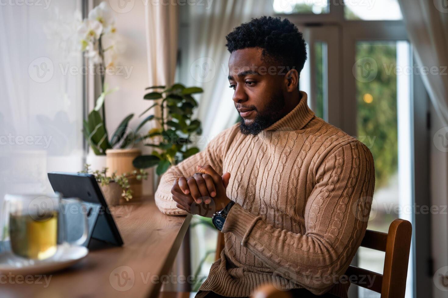 Pensive African man engaged in virtual meeting, using technology to communicate during freelance work at bar. photo